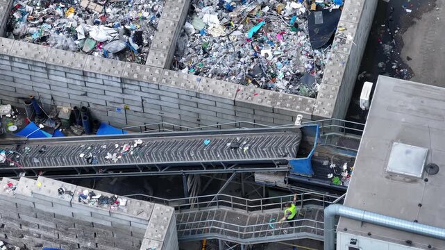 Plastic waste moves along a conveyor belt for sorting and processing. Workers monitor and manage the flow of materials. Industrial equipment separates recyclable items from waste.