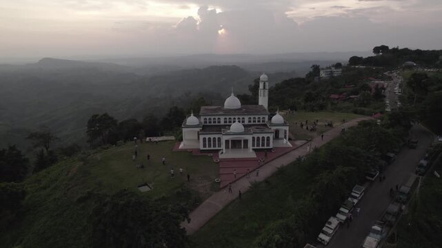 Drone view of a white hilltop mosque in Sajek Valley during a moody sunset
