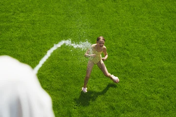A cheerful child plays with water sprinklers in the garden during the summer. Creatively watering the garden—with fun and high spirits. An authentic, real little girl. © Igor