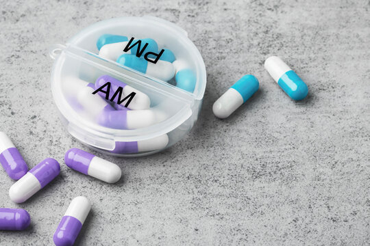 Capsule pills with daily pill box on a grey concrete background. Healthcare and medication concept, copy space