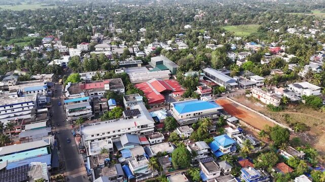 Cinematic aerial view of a thriving town in Kerala showcasing rooftop solar panel installations integrated into residential and commercial buildings, surrounded by lush coconut groves and vibrant trop