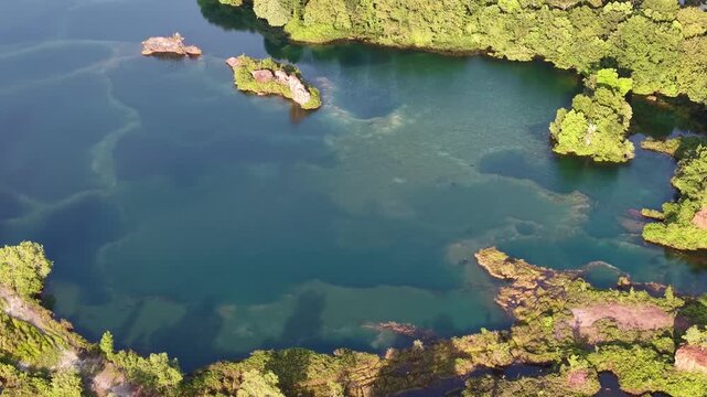 Aerial footage of an abandoned quarry lake with vegetated islets and surrounding forest.