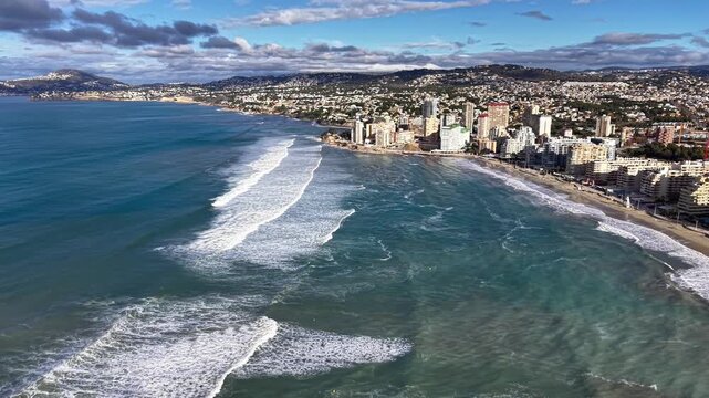 Aerial coastal panorama with gentle waves and urban skyline, wide angle view shows shallow reef patterns