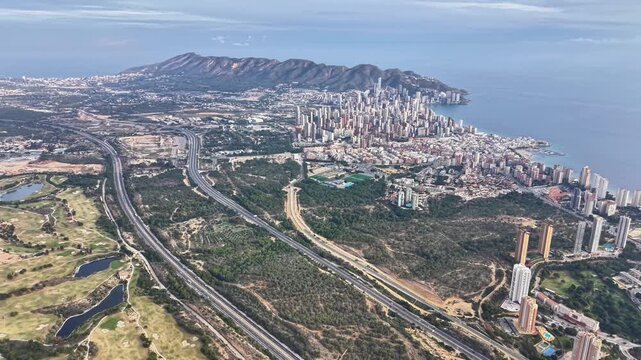 Drone aerial view of highway approach to coastal city, visible interchanges, bayfront towers and mixed