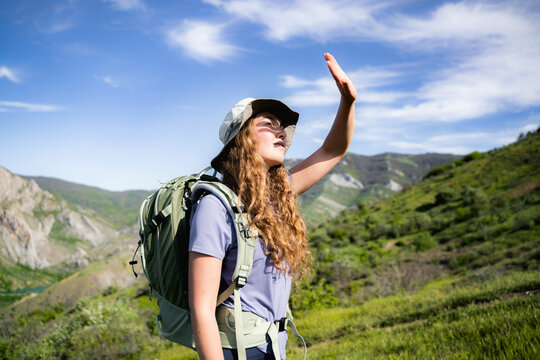 Side view portrait of a young woman with a backpack covering her eyes from sunlight during a mountain hike on a sunny day.
