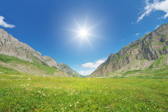 Mountain valley landscape under a vibrant blue sky with the bright sunburst shining down