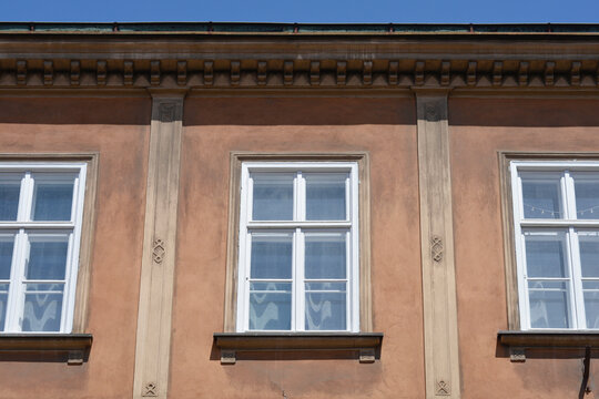 A horizontal medium shot of a brown historic building facade with white wooden windows and decorative pilasters