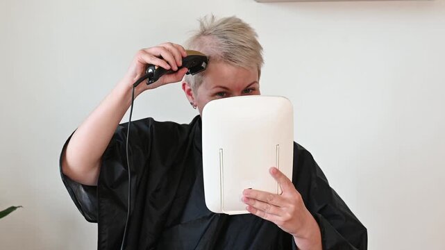 A woman shaves her hair with a trimmer. Balding hair loss due to chemotherapy. Baldness in women during cancer treatment. Toxic effects of chemotherapy drugs on hair.