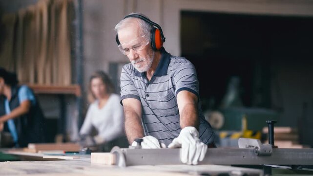 Experienced male woodworker using a table saw to cut a piece of wood. Skilled carpenter wearing safety equipment while working in his shop