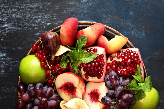 Colorful dish with fruits and berries on platter. Assorted fruits on plate. Pomegranates, figs, peaches, grapes and other fruits on platter. Red currant and mint pour with fruit. Copy space. Top view