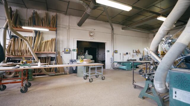 Male instructor teaching a female apprentice how to use a table saw. Other workers are moving materials in the large carpentry shop