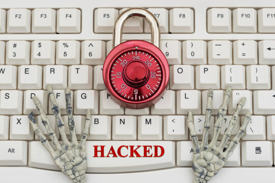 Hacked text with skeleton hands with combination lock on a white computer keyboard for cybersecurity