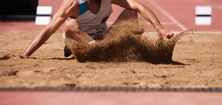 Male athlete long jump landing sand spray, landing in long jump in track and field