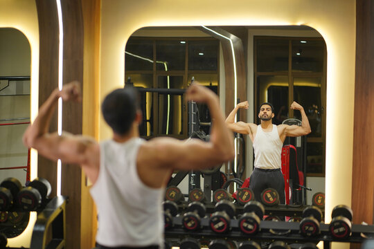 Sion, Mumbai, India-22nd March 2026-Muscular young man flexing his biceps in front of a gym mirror after an intense strength training session.