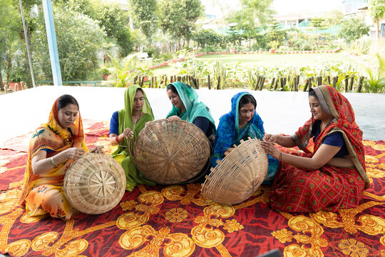 A group of skilled Indian rural women artisans weaving traditional bamboo baskets together during a handicraft training session. Women in colorful sarees working collaboratively on sustainable.