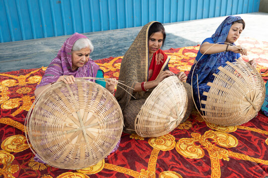 Skilled Indian village women crafting bamboo baskets by hand in a rural setting. Represents traditional craftsmanship, self-help groups, vocational skills, sustainable products, women artisans.
