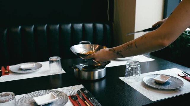 Tattooed waitress serving a hot wok dish on a portable burner. A modern all you can eat sushi buffet with a table elegantly set