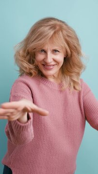 Beautiful mature woman in a pink sweater blowing a kiss and then making a heart gesture with her hands, smiling at the camera