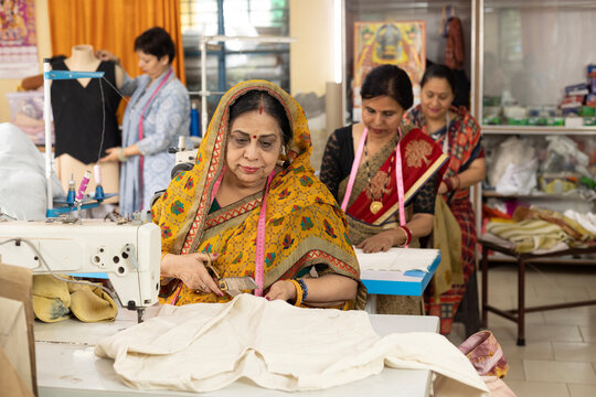 Indian Senior Woman Cutting Fabric with Scissors in a Garment Export House Factory
