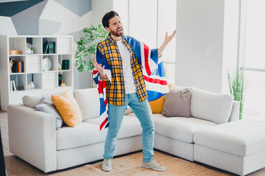 Man wrapped in Union Jack flag cheering ecstatically in living room while watching sports and celebrating at home