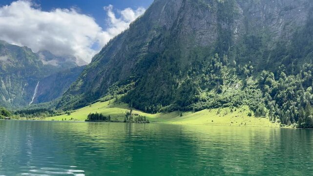 Panoramic, scenic view of Konigssee Lake. Rothbach waterfall in the background. Salet stop where route to Obersee starts. View from a moving boat. Chrystal clear water. Konigssee, Bavaria, Germany