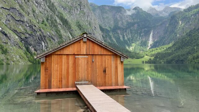 Panoramic, scenic view of Obersee Lake. Ficherhutte wooden boathouse in front. Mountains and Rothbach waterfall in the background. Chrystal clear water. Obersee, Bavaria, Germany