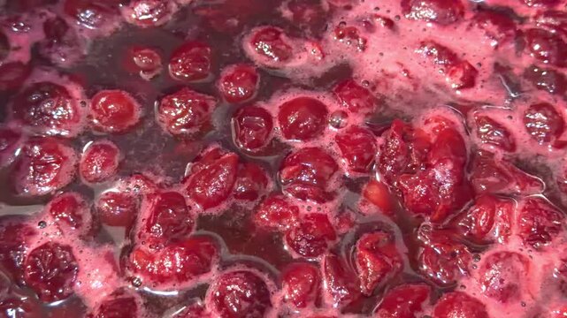 Boiling cherry jam with berries in dark syrup and foam in close up