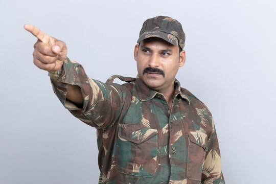 Portrait of angry indian army soldier pointing finger to other side in uniform standing with copy space isolated on gray studio background
