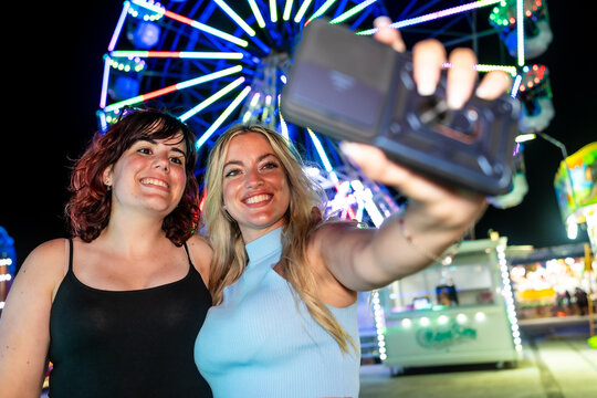 Young friends taking selfie at amusement park with ferris wheel lights