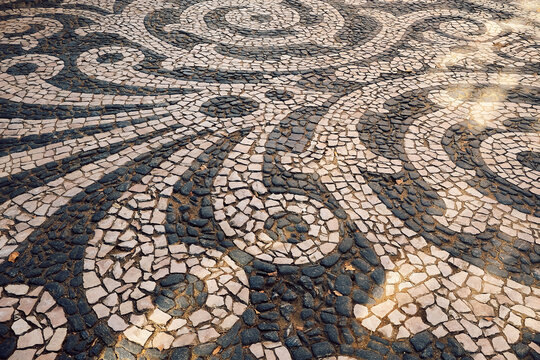 Pattern of stones on  sidewalk in  city. daylight hours showing artistic design. sidewalk features a design made of various stones arranged in curves and swirls. artwork  pavement patterns during day