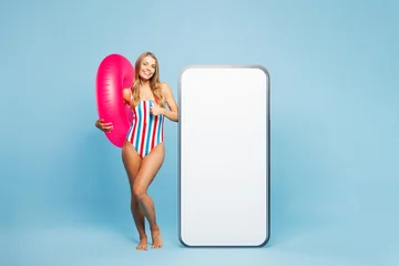 Full body young fun woman wear bikini swimsuit rest near hotel pool big huge blank screen area mobile cell phone show thumb up isolated on plain blue background. Summer vacation sea sun tan concept. © ViDi Studio