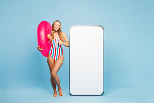 Full body young fun woman wear bikini swimsuit rest near hotel pool big huge blank screen area mobile cell phone show thumb up isolated on plain blue background. Summer vacation sea sun tan concept.