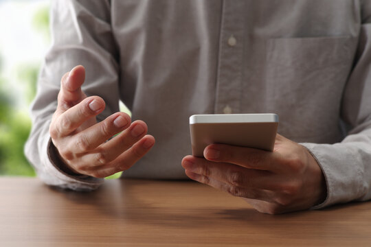 Man talking on smartphone app at table. Looking at mobile screen.