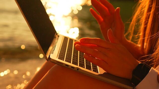 Laptop sunset beach woman typing on a portable computer while sitting on the sand during a vibrant golden hour