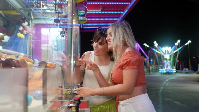 Cheerful young women playing claw machine game at amusement park