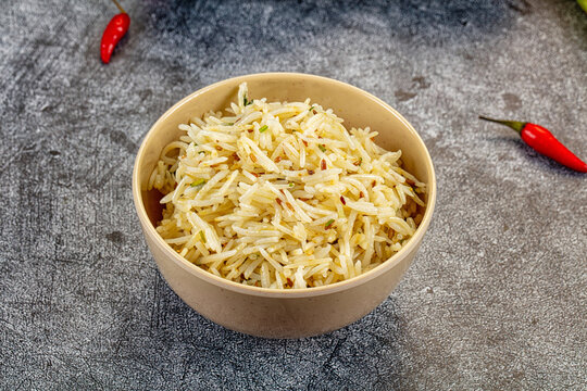Bowl of seasoned basmati rice with cumin seeds and red chili peppers on dark textured background