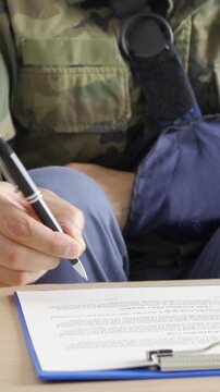 Front view of a disability soldier with sling signing contract at office