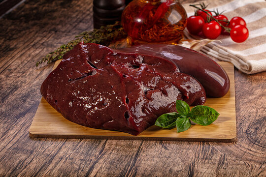Raw beef liver and kidney on wooden board with fresh herbs and tomatoes