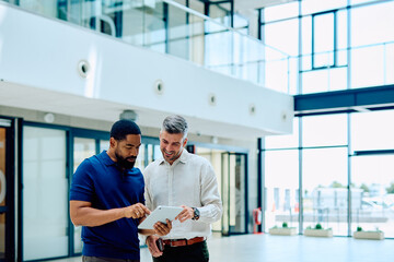 Fototapeta premium Two diverse businessmen collaborating on a project, analyzing data on a tablet in a contemporary office setting, sharing ideas