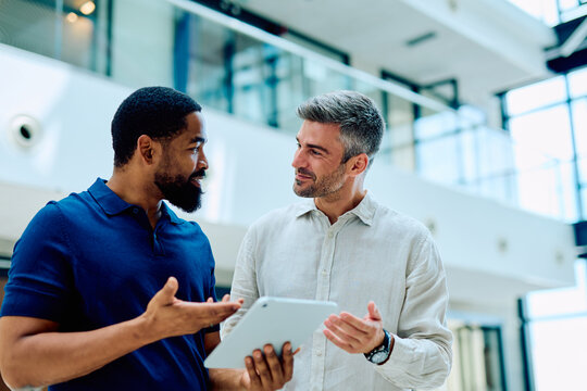 Two diverse business colleagues standing in a modern office, having a serious discussion while looking at a digital tablet