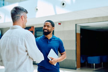 Fototapeta premium Two diverse business professionals handshaking, smiling and collaborating in a modern office hallway, symbolizing agreement and partnership