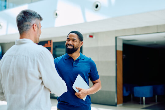 Two diverse business professionals handshaking, smiling and collaborating in a modern office hallway, symbolizing agreement and partnership
