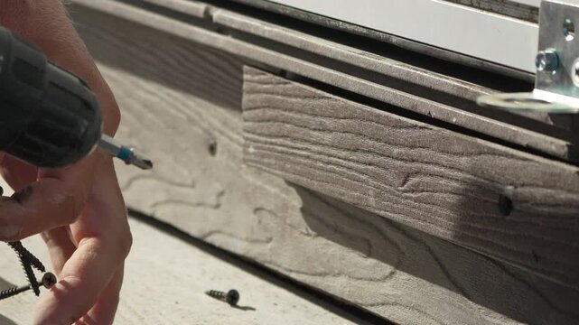 Drill screw construction, builder installing wood planks on outdoor deck for home renovation project during a sunny day of manual labor