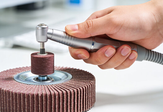 Hand using rotary tool on abrasive flap wheel in a clean practical workshop setting