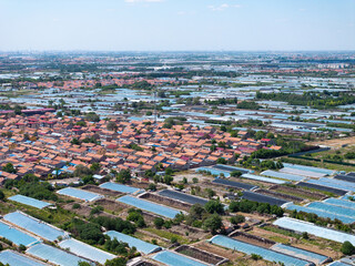 Fototapeta premium Aerial view of rural Rizhao with red-tiled houses and rows of agricultural greenhouses
