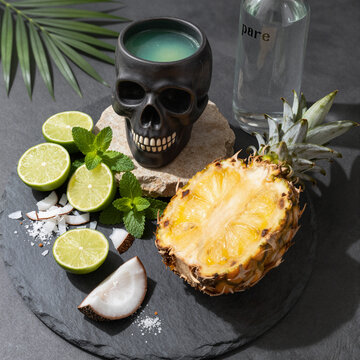tropical cocktail with pineapple and coconut on dark slate serving board in halloween skull mug