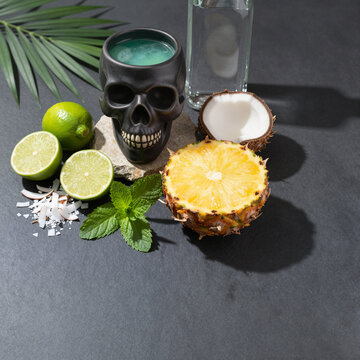 tropical cocktail in skull mug with sliced lime, pineapple, coconut on dark surface summer refreshment