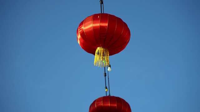 Slowmo footage of red Chinese lanterns hanging on strings against a clear blue sky