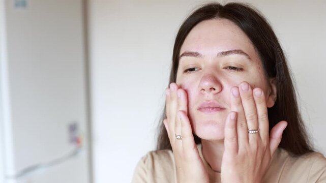 Young Caucasian woman applies serum and massages face. Close up slow motion shows skincare routine for problem skin. Healthy beauty care concept.