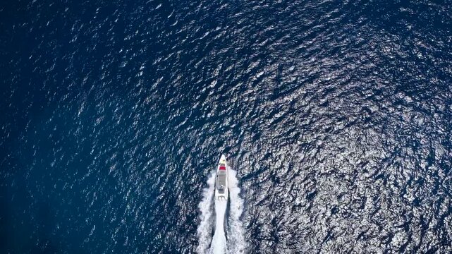 High aerial overhead view of a motor boat cruising with high speed over turquoise, sparkling ocean